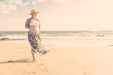 Relaxed pregnant woman holding hand on belly. Cheerful future mother walking on beach during vacation. Pregnancy concept