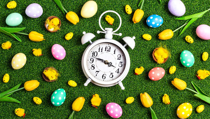 Easter alarm clock with colorful eggs and tulips on a green grass background.