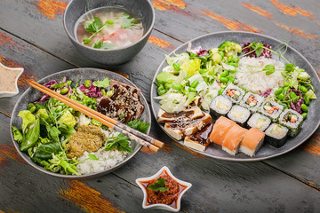 Close up pan-Asian dishes in bowls. Rice with spices and beef, salad with beans, rolls with salmon and avocado, fish soup. Tasty and healthy nutrition