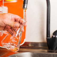 A man pours tap water into a glass flask.