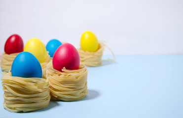 Easter eggs of blue, red, yellow color stand in pasta nests on a blue white background horizontal background