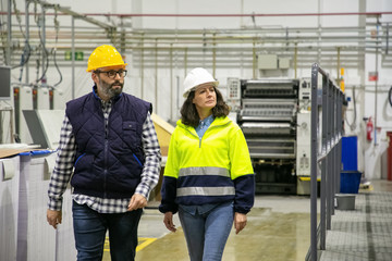 Front view of two technicians inspecting printing factory. Confident employees walking near printing machine. Print manufacturing concept
