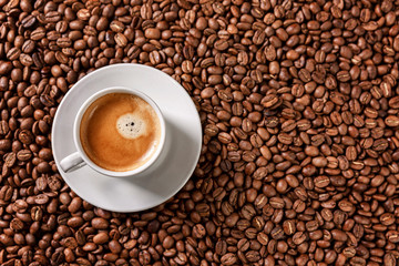 A white cup with aromatic coffee stands on scattered grains. View from above.