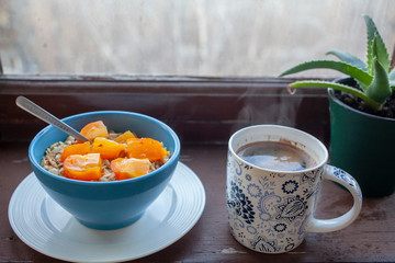
Oatmeal with orange persimmons, coffee, plant on a windowsill