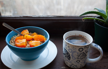 
Oatmeal with orange persimmons, coffee, plant on a windowsill