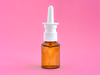 Nasal spray in a glass vial on a pink background. Treating flu, colds, or allergies.