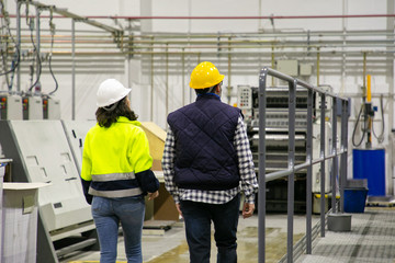 Back view of two factory employees walking at plant. Rear view of man and woman walking at printing house. Print manufacturing concept