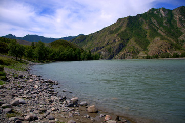 The rocky shore of a mountain turquoise river at a bend at the foot of high mountains.