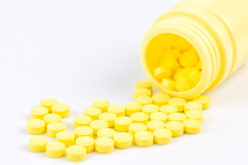 Selective focus of yellow medicine pills and tablets spilling out of a drug bottle on white background with copy space for your text..