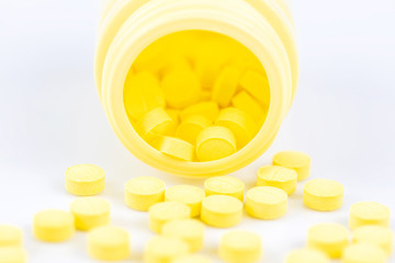 Selective focus of yellow medicine pills and tablets spilling out of a drug bottle on white background..