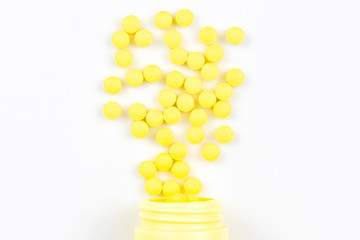 Selective focus of yellow medicine pills and tablets spilling out of a drug bottle on white background..