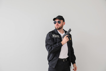 Male police officer with gun on light background