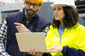 Closeup view of workers talking while standing with laptop. Confident technicians discussing working process. Manufacturing concept
