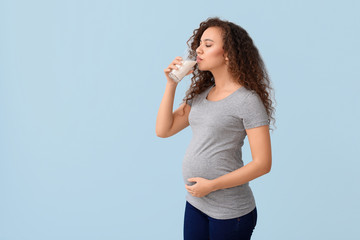 Young pregnant African-American woman with milk on color background