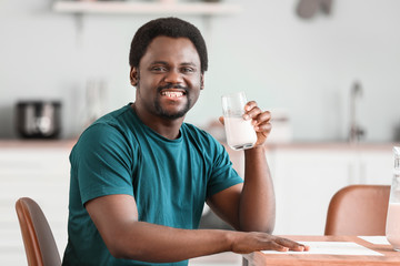 Young African-American man with milk in kitchen