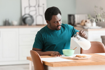 Fototapeta na wymiar Young African-American man with milk and flakes in kitchen
