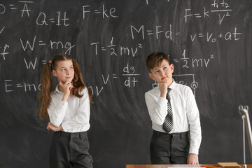 Thoughtful little children near blackboard at physics lesson in classroom