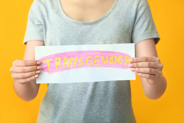 Woman holding paper with text TRANSGENDER on color background