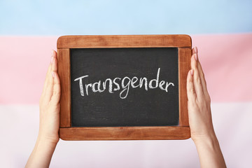 Female hands holding chalkboard with text TRANSGENDER on color background