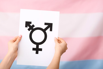 Female hands holding paper with drawn symbol of transgender on color background