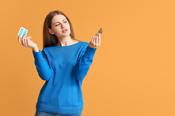 Young woman with birth control pills and condom on color background