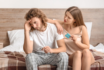 Sad young couple with oral erectile dysfunction medication and condom in bedroom