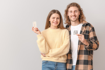 Young couple with birth control pills and condom on light background
