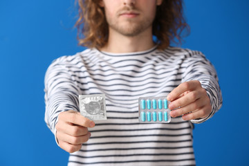 Young man with oral erectile dysfunction medication and condom on color background