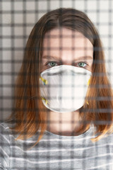 Coronavirus. Young woman in protection mask behind bars in a jail cell. Patient isolated to prevent...