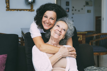 Happy middle aged woman hugging senior lady in living room. Mother and daughter embracing each other at home. Happy family concept