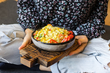 Woman hold vegan lunch, vegetarian dinner in bowl in hands on her legs. Couscous with vegetables in bowl