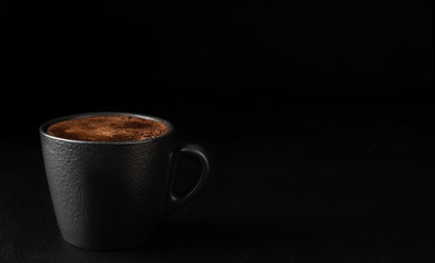 A cup of espresso with foam. Black stone background. Copy space for text. Close-up, shallow depth of field. Morning hours waiting for coffee.