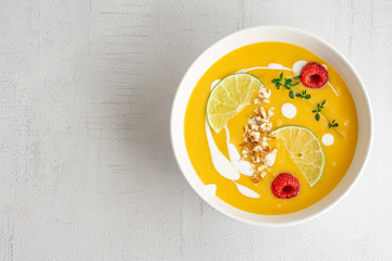 Pumpkin cream soup decorated with nuts, sour cream, lime, raspberries olive oil, pepper. Top view. Isolated. Copy space. Vegetarian, healthy food, diet, recipe or menu concept. Grey background