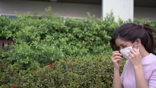 4k Young asian woman put on mask while walking by the green palnt bushes, health and medical concept, co2 fresh air oxygen, Air polluted issues, Corona virus 2019, covid, transmitted disease control