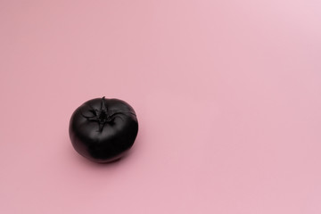 Matte black tomato on the pink background. The object is at the left side of the picture. Minimal style. Conceptual minimalism. Matte surface. Fruit. One. Copy space