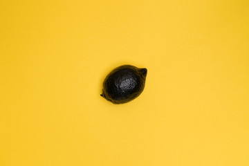 Black lemon on the yellow background. Minimal style. Top view. The lemon at the centre of the frame. Minimal art. Fruit. One