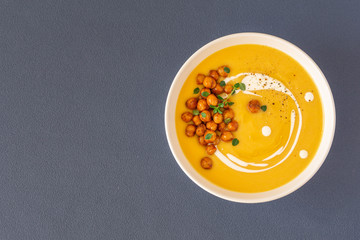 Pumpkin cream soup decorated with spicy chickpeas, sour cream, olive oil, pepper. Top view. Isolated. Copy space. Vegetarian, healthy food, diet, recipe or menu concept. Dark grey background. 
