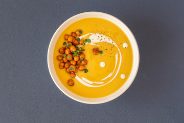 Pumpkin cream soup decorated with spicy chickpeas, sour cream, olive oil, pepper. Top view....