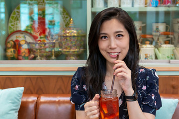 Happy woman sipping a drink in the cafe. Closeup Asian women are drinking iced coffee during breaks. The girl drinks from a glass through a straw. Young girl drinking Ice tea cocktail with a straw.