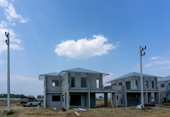 Construction progress in a real estate property project site, people are building the precast house on the brown land, electricity post in the front, working in a hot day under cloudy sky