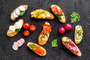 Sandwiches - set with vegetables, caviar, salami - on black background top-down