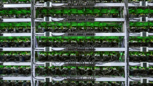 Cryptocurrency mining equipment on large farm. ASIC miners on stand racks mine bitcoin in server room. Blockchain techology application specific integrated circuit. Steadycam camera moves back away.
