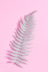 fern leaf in glitter sequins. simple minimalistic composition on a pink background. top view, vertical frame