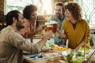 Happy friends toasting with beer at dining table.