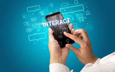 Female hand typing on smartphone with INTERACT inscription, social media concept