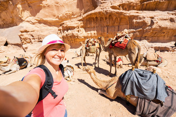 Tourist making selfie with camels in desert.