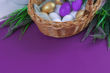 Happy Easter Day.Greeting card or banner for sale of a store or website.Golden, white, purple eggs in a basket on a purple background next to a bouquet of greenery.Provence.Copy space.Top view