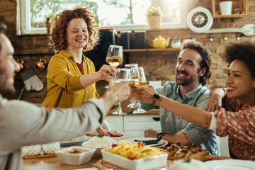 Happy friends toasting with wine while having lunch together at home.