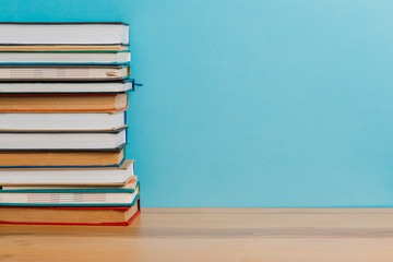 A simple composition of many hardback books, raw books on a wooden table and a bright blue background. Going back to school. Copy space. Education.