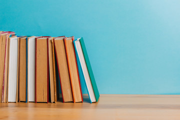 A simple composition of many hardback books, raw books on a wooden table and a bright blue background. Going back to school. Copy space. Education.